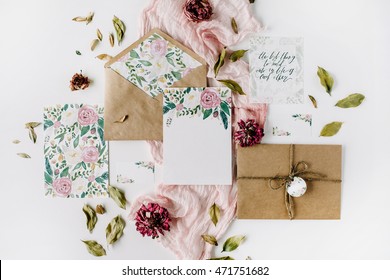 Workspace. Wedding Invitation Cards, Craft Envelopes, Pink And Red Roses And Green Leaves On White Background. Overhead View. Flat Lay, Top View