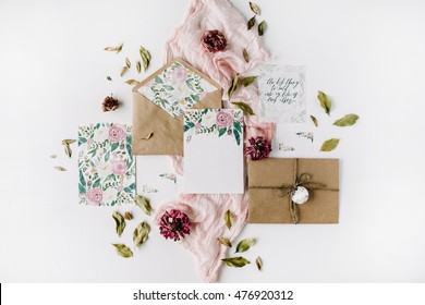 Workspace. Wedding Invitation Cards, Craft Envelopes, Pink And Red Roses And Green Leaves On White Background. Overhead View. Flat Lay, Top View