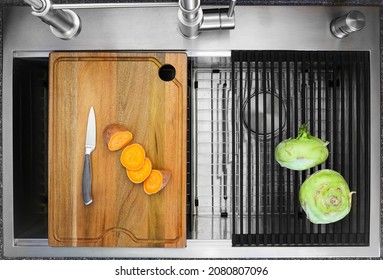 Workstation kitchen sink with cutting board and draining rack used to slice a sweet potato and to dry kohlrabi vegetable - Powered by Shutterstock