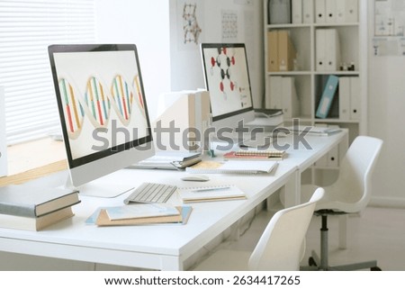 Workstation in modern lab showing computer screens with scientific patterns and research books on desk. Clean and organized lab environment without people