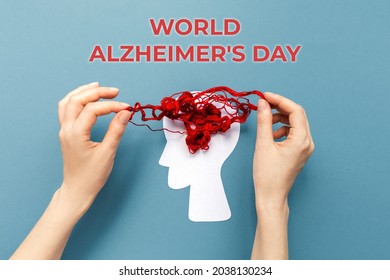 World Alzheimer's day. Female's hands unravel the tangled red threads on the silhouette of the head, representing the brain. Blue background. Flat lay. The concept of mental health.