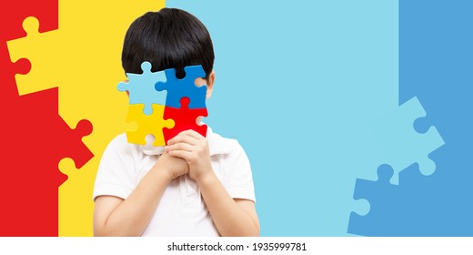 World autism awareness day April 2 - Studio Portrait of a cute asian boy cover his face with the colorful puzzles pieces. Autism Spectrum Disorder concept, ASD, Syndrome, Light it up blue, Backdrop.