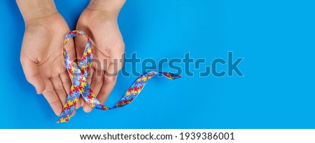 World Autism awareness day. Autistic boy hands holding puzzle pattern ribbon on blue background