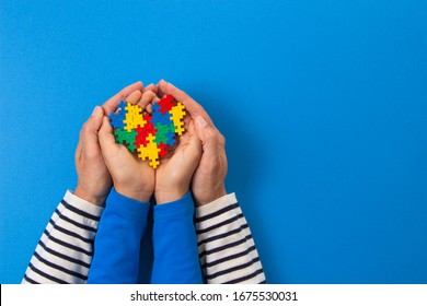World autism awareness day concept. Adult and child hands holding puzzle heart on light blue background