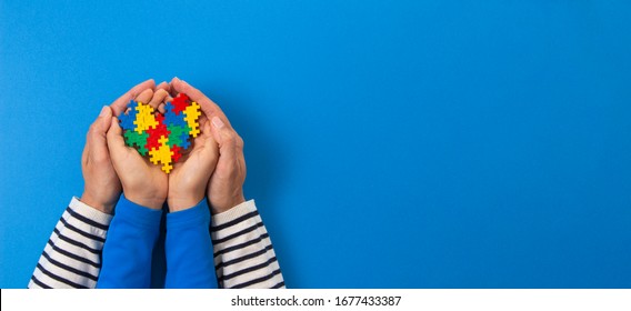 World Autism Awareness Day Concept. Adult And Child Hands Holding Puzzle Heart On Light Blue Background