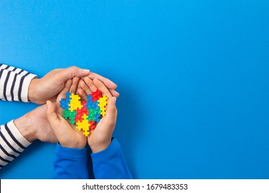 World Autism Awareness Day Concept. Adult And Child Hands Holding Puzzle Heart On Light Blue Background