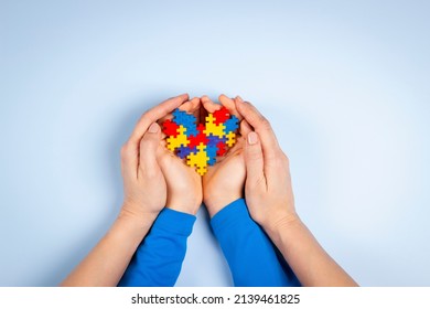 World Autism Awareness Day Concept. Adult And Child Hands Holding Puzzle Heart On Light Blue Background. Top View
