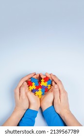 World Autism Awareness Day Concept. Adult And Child Hands Holding Puzzle Heart On Light Blue Background. Top View