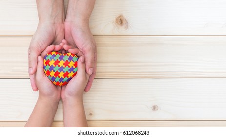 World Autism Awareness day, mental health care concept with puzzle or jigsaw pattern on heart with autistic child's hands supported by nursing family caregiver 