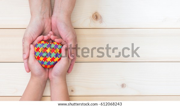 World Autism Awareness day,\
mental health care concept with puzzle or jigsaw pattern on heart\
with autistic child\'s hands supported by nursing family caregiver\
