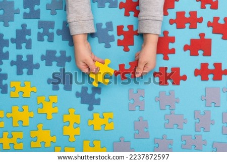 World Autism Awareness Day or month concept. Creative design for April 2. Color puzzle, symbol of awareness for autism spectrum disorder on blue background. Children's hands and Jigsaw puzzle