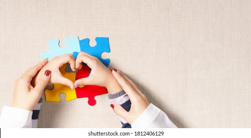 World autism awareness day, understanding  love concept, a beautiful mother holding hands of little autistic child making heart shape over symbol colored puzzle. ASD, April 2, Top view banner. - Powered by Shutterstock