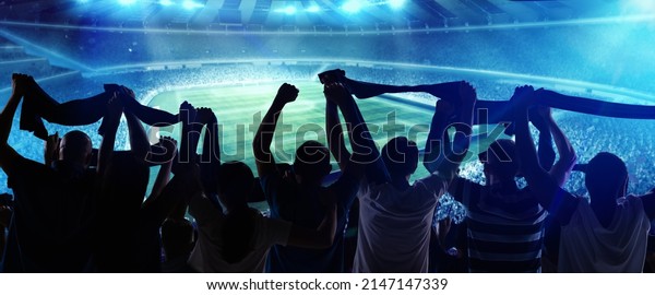 At\
world cup. Back view of football, soccer fans cheering their team\
with state flags and scarfs at crowded stadium at evening time.\
Concept of sport, cup, world, team, event,\
competition