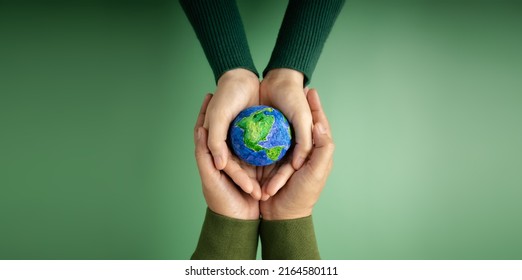 World Earth Day Concept. Green Energy, ESG, Renewable and Sustainable Resources. Environmental Care. Hands of People  Embracing a Handmade Globe. Protecting Planet Together. Top View