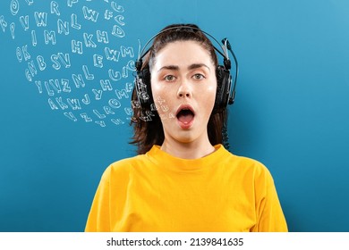 World English Language Day. Portrait of a young woman wearing headphones, with her mouth open. Blue background with letters. The concept of learning foreign languages.