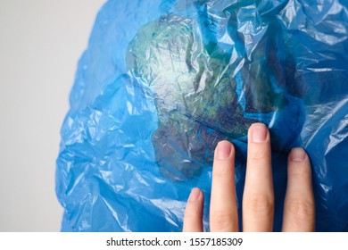 World Environment Day Concept. World Globe In A Blue Plastic Bag. Environmental Pollution. The Planet Is In Danger. The Human Hand Is Trying To Save The World