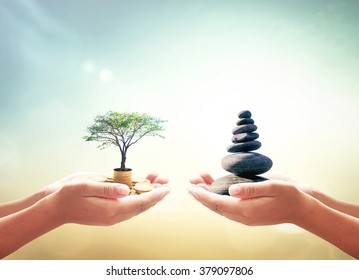 World Environment Day Concept: Two Human Hands Holding Stacks Of Golden Money With Big Tree And Zen Stones On Blurred Nature Background