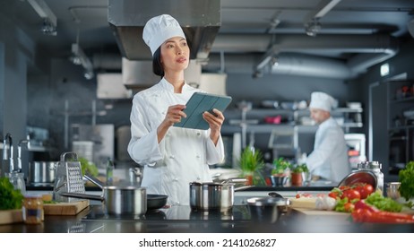 World Famous Restaurant: Asian Female Chef Cooking Delicious and Authentic Food, Uses Digital Tablet Computer While Working in a Modern Professional Kitchen. Preparing gourmet organic Dishes - Powered by Shutterstock