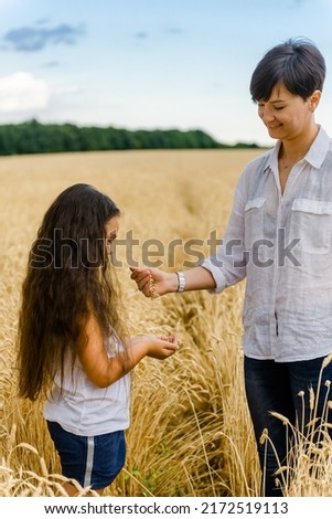 World food crisis. Deficit of grain in the world markets. A girl with her mother stands in a wheat field. Woman pouring grains of wheat into the hands of her daughter