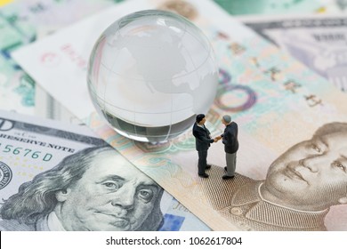 World Or Global Financial Tariff Trade War Negotiation Talk, Collaboration Or Discuss Concept, Miniature People Businessman Leader Handshaking On Chinese Yuan Banknotes And US Dollar.