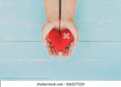 World Health Day, Healthcare And Medical Concept. Woman Hand Holding Red Heart With Stethoscope, Notepad Or Notebook, Thermometer And Yellow Pill On Pastel White And Blue Wooden Table Background.