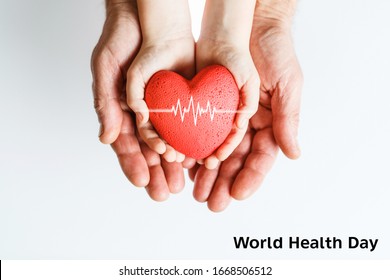 World Health Day. Male Hands Hold Childrens Palms With A Red Heart In Them. The Concept Of Family Love And Support. On A Light Background. Studio Photo.