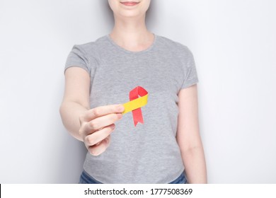World Hepatitis Day concept. Girl in gray T-shirt holds in her hand awareness symbol red-yellow ribbon. Gray background - Shutterstock ID 1777508369