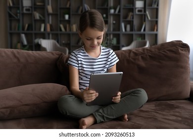 World of information. Curious kid preteen girl sit on sofa alone hold digital pad using gadget for learning browsing social networks chatting. Cute tween child schoolgirl play game on tablet pc online