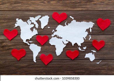 World map cutted from white paper and red felt hearts on the wooden background. Love and peace concept. Flat lay, top view, copy space, mock up, toned