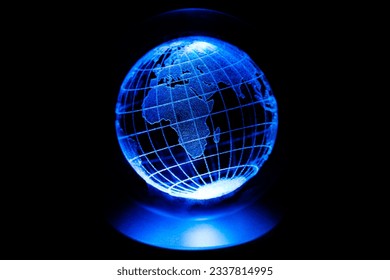 World map model engraved with a laser inside a glass globe. World map with blue neon light on isolated black background. Asian and African continents are in the foreground. Earth and finance concept.