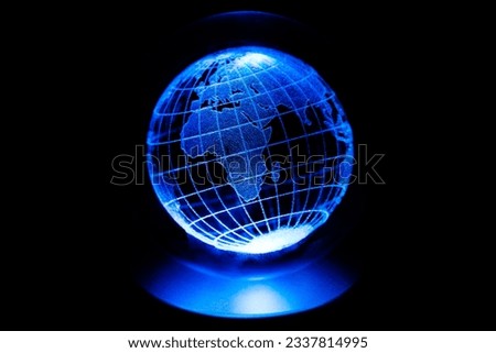 World map model engraved with a laser inside a glass globe. World map with blue neon light on isolated black background. Asian and African continents are in the foreground. Earth and finance concept.
