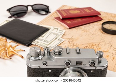 World Map, Two Passports, A Magnifying Glass, Money In A Black Leather Wallet, An Old Film Camera, Sunglasses And A Shell On A White Table. Selective Focus. Inscription - Passport Russian Federation