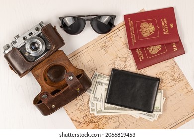 world map, two passports, money in a black leather wallet, an old film camera in a leather case and sunglasses on a table. view from above. selective focus. inscription - passport Russian Federation