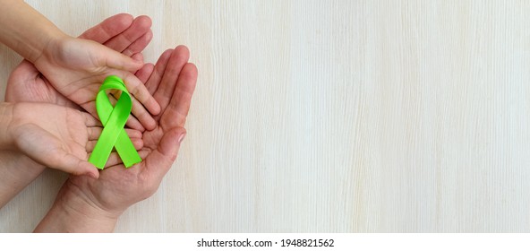 World Mental Health Awareness Day.Adult And Child Hands Holding Green Ribbon On White Panoramic Background.Organ Donation.World Kidney Day. Banner. Copy Space. Top View. Mock Up