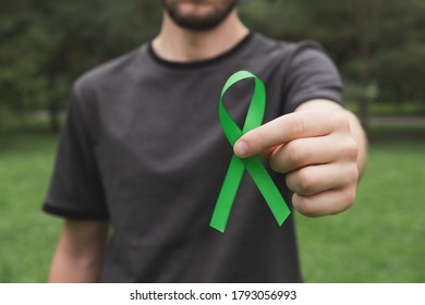 World Mental Health Day Concept. Man Hands Hold Green Awareness Ribbon. Close Up