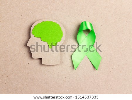 World mental health day concept. Green awareness ribbon and brain symbol on a brown background.