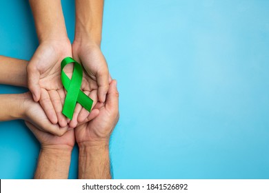 World Mental Health Day; green ribbon put in human's hands on blue background - Shutterstock ID 1841526892
