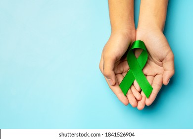 World Mental Health Day; green ribbon put in human's hands on blue background - Shutterstock ID 1841526904