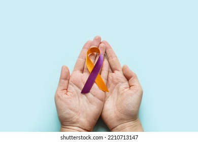 World Psoriasis Day. Woman's hands are holding a purple-orange ribbon on blue background. Treatment of skin diseases, dermatitis, eczema, psoriasis. Medical banner - Shutterstock ID 2210713147