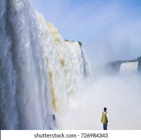 The World Of Roaring Water. Elderly Tourist - Woman With A Backpack Watching The Waterfall. Iguazu Falls In South America. Concept Of Active And Extreme Tourism