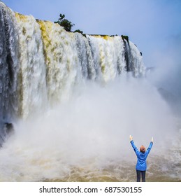 The World Of Roaring Water. Iguazu Falls In South America. Elderly Woman - Tourist Is Shocked By A Waterfall. Concept Of Active And Extreme Tourism