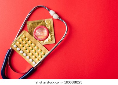 World sexual health or Aids day, Top view flat lay condom in wrapper pack, birth control pill and doctor stethoscope, studio shot isolated on a pink background, Safe sex and reproductive health