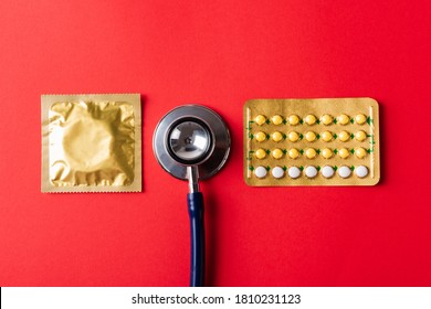 World Sexual Health Or Aids Day, Top View Flat Lay Condom In Wrapper Pack, Birth Control Pill And Doctor Stethoscope, Studio Shot Isolated On Red Background, Safe Sex And Reproductive Health Concept