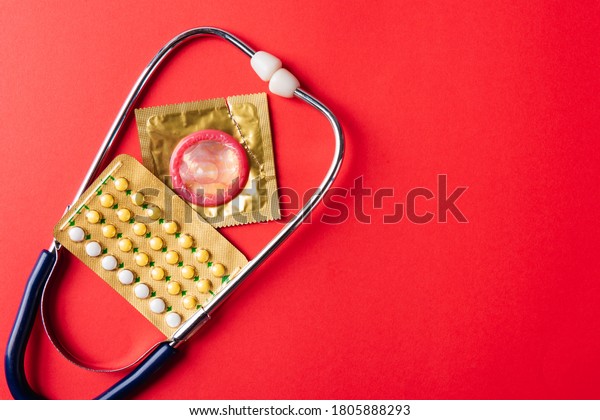 World sexual health or Aids day, Top view flat lay\
condom in wrapper pack, birth control pill and doctor stethoscope,\
studio shot isolated on a pink background, Safe sex and\
reproductive health