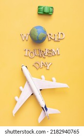World Tourism Day text from wooden letters with globe, car and airplane on yellow background. Top view, flat lay.