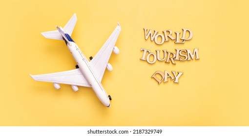 World Tourism Day text from wooden letters on a yellow background with airplane top view, flat lay