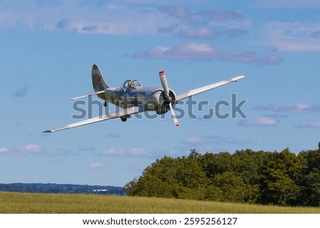 A World War Two era Soviet propeller fighter plane takes off  from a grassy airfield against a beautiful partly cloudy blue sky on a sunny day