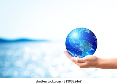 World Water Day And Global Warming Concept . A Hand Holding Earth Ball Shape On Blue Sea Bokeh Background. Copy Space On Horizontal Sheet. Elements Of This Image Furnished By NASA.