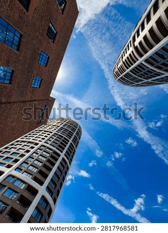 Worms eye view of oval towers and brick wall. Tall modern skyscrapers and an old brick facade point directly toward the center of a cloudy blue sky.