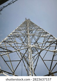 Worm's eye view perspective of a tall metal truss radio transmission tower with steel grid structure and barbed wire fence in foreground under clear daylight.